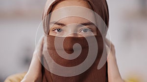 Headshot of charming confident Muslim woman with closed face and brown eyes looking at camera. Portrait of beautiful