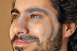 Headshot. Close up portrait of young well-groomed man looking away against beige studio background. Men's personal