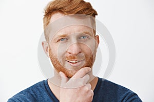 Headshot of creative and intrigued attractive redhead guy with bristle, rubbing beard and smirking, having great plan or