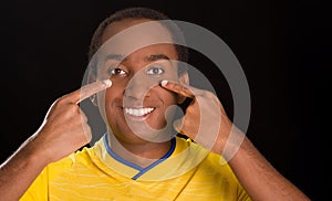 Headshot dark skinned male wearing yellow football shirt in front of black background, using fingers applying facepaint
