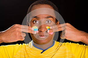 Headshot dark skinned male wearing yellow football shirt in front of black background, using fingers applying facepaint