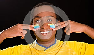 Headshot dark skinned male wearing yellow football shirt in front of black background, using fingers applying facepaint