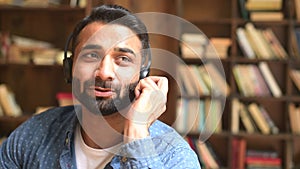 Headshot of focused indian male employee wearing headset takes a call