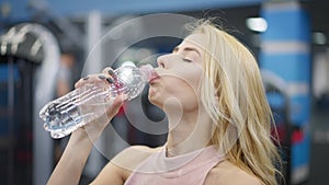 Headshot of gorgeous Caucasian blond woman drinking water in gym and looking at camera. Confident beautiful millennial