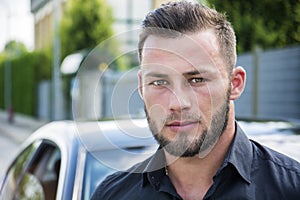 Headshot of handsome bearded man next to car