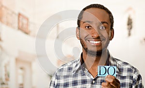 Headshot handsome man holding up small letters spelling the word do and smiling to camera