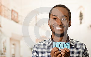 Headshot handsome man holding up small letters spelling the word joy and smiling to camera