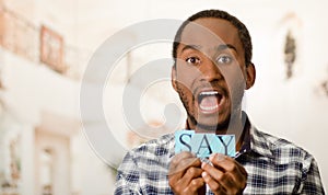Headshot handsome man holding up small letters spelling the word say and showing dramatic facial expression to camera