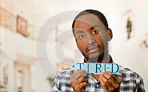 Headshot handsome man holding up small letters spelling the word tired and looking to camera