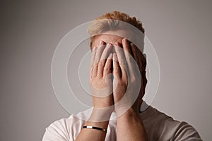 Headshot of a handsome young man sitting with hands on the face. Stress, issues.