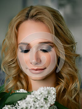 Headshot of happy beautiful blonde woman with lilac flower bouquet closed eyes gorgeous trendy makeup beauty shiny skin posing