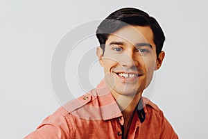 Headshot hispanic latino man black hair smiling handsome young adult wearing melon shirt over gray background looking at