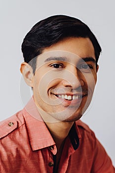 Headshot hispanic latino man black hair smiling handsome young adult wearing melon shirt over gray background looking at