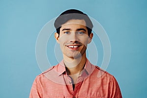 Headshot hispanic latino man black hair smiling handsome young adult wearing pink shirt over blue background looking at