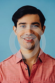 Headshot hispanic latino man black hair smiling handsome young adult wearing pink shirt over blue background looking at