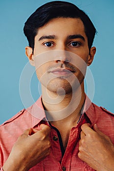 Headshot hispanic latino man black hair smiling handsome young adult wearing pink shirt over blue background looking at