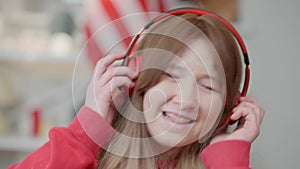 Headshot of joyful Asian redhead teen girl in headphones dancing and singing indoors. Close-up portrait of happy