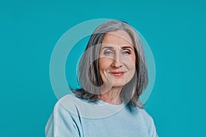 Headshot of mature beautiful woman looking at camera and smiling while standing against blue background