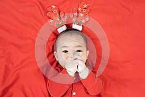 Headshot of 6 months old cute newborn baby boy wearing christmas antlers of a deer on a red blanket.Looking at camera. Holiday