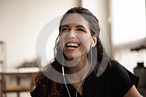 Headshot of overjoyed laughing millennial latina female wearing wired earphones