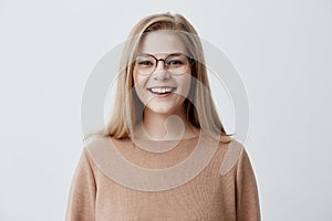 Headshot of pleasant-looking young Caucasian woman wearing eyeglasses with broad smile showing her straight white teeth