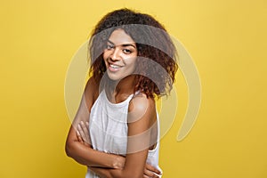 Headshot portrait of beautiful attractive African American woman posting crossed arms with happy smiling. Yellow studio