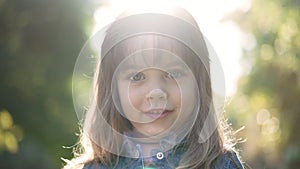 Headshot portrait of charming happy Caucasian little girl posing in sunrays outdoors. Cute smiling child looking at