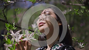 Headshot portrait of confident beautiful Asian young woman posing at blooming tree with white flowers in sunlight