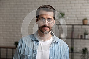 Headshot portrait of confident millennial male wearing glasses posing indoors