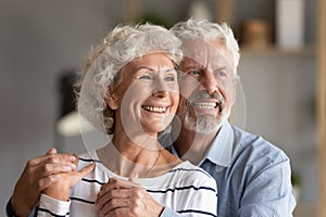 Headshot portrait happy 60s couple hugging standing indoors look away