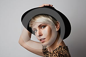 Headshot Portrait of happy blonde girl with black hat smiling looking at camera. White background. Profile view