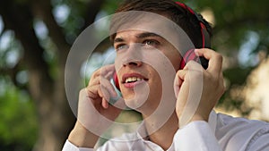 Headshot portrait happy smiling young man in headphones singing dancing listening to music outdoors. Close-up handsome