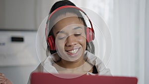 Headshot portrait of joyful young African American woman greeting in video chat waving and talking at laptop web camera