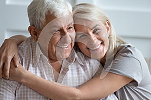 Headshot portrait of loving elderly couple hugging at home