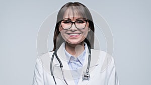 Headshot portrait of smiling female doctor on gray background