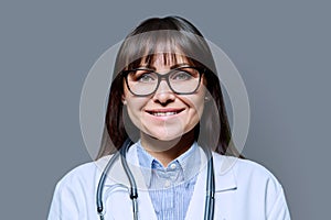 Headshot portrait smiling female doctor looking at camera on gray background