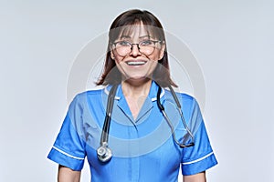 Headshot portrait of nurse in blue uniform looking at camera on light studio background