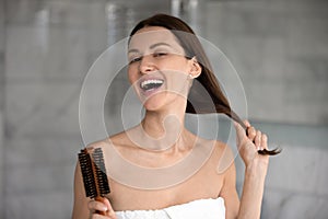 Headshot portrait woman holding hairbrush combing her strong healthy hair
