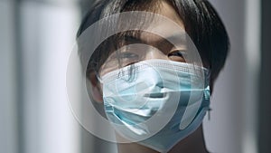 Headshot portrait of young Asian man in Covid-19 face mask looking at camera in sunlight. Close-up face of serious