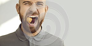 Headshot portrait of a young man with healthy teeth trying to crack a hard walnut