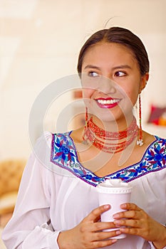 Headshot pretty young woman wearing traditional andean blouse, holding white coffee mug, facing camera, beautiful smile