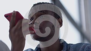 Headshot of serious African American man talking at smartphone speakerphone looking away. Close-up portrait of young