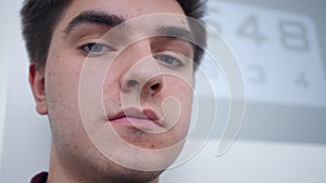 Headshot of serious man looking at camera with blurred optometric chart at background. Close-up portrait of Caucasian