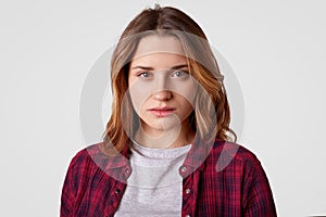 Headshot of serious woman has confident expression, wears checkered shirt, casual t shirt, stands against white background,