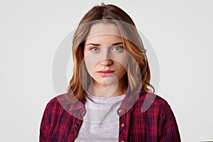 Headshot of serious woman has confident expression, wears checkered shirt, casual t shirt, stands against white background, photo