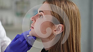 Headshot side view of slim young woman in beauty salon with male hand marking chin for filler injection. Caucasian