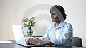 Headshot of smiling indian male employee wearing headset takes a call