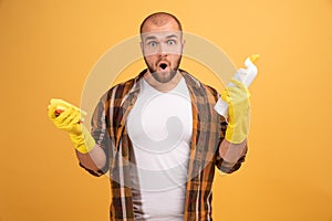 Headshot of surprised Caucasian young man looks in amazement, wears casual clothes, holds rag and bottle of detergent, has much