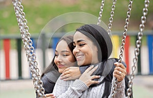 Headshot of two happy young women hugging on a swing