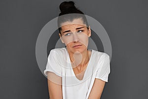 Headshot of unhappy young brunette woman feeling apologize for doing something wrong, looking at one side with brows frowned. Sad